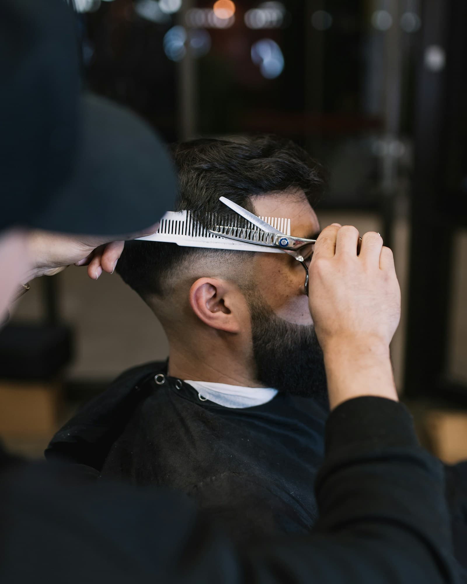 A barber checking a fade with a comb and shears.