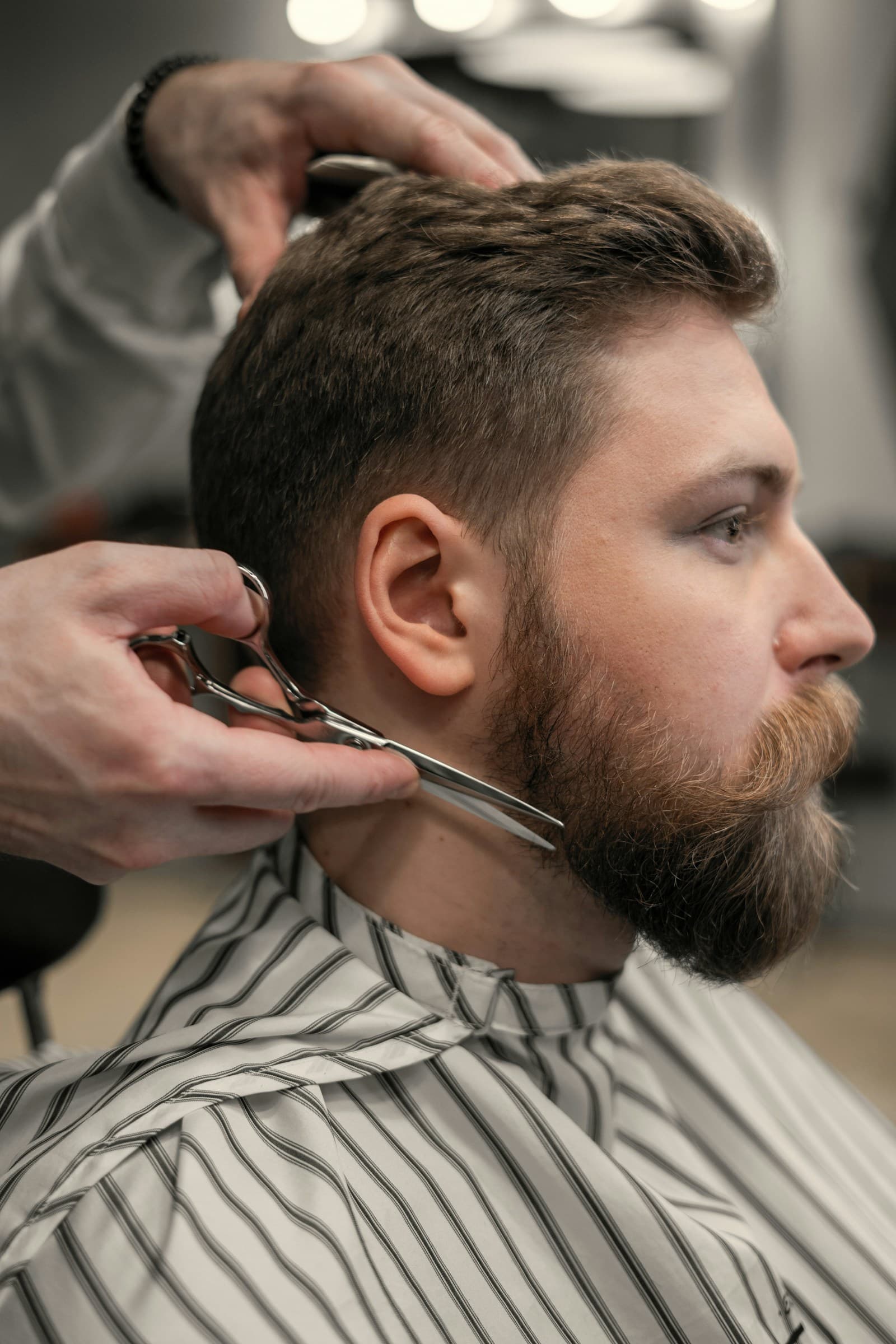 A barber trimming a client's beard with shears.